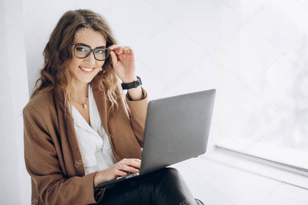 Young beautiful business woman in glasses works on laptop in her office