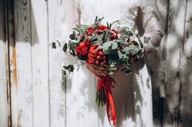 Beyaz bir elbise içinde gelin düğün buket kırmızı gül ve yeşil ve kırmızı kurdele ile düzenliyor