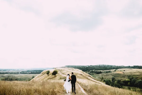 美丽的新婚夫妇走在球场上的道路上 他们的婚礼当天 — 图库照片