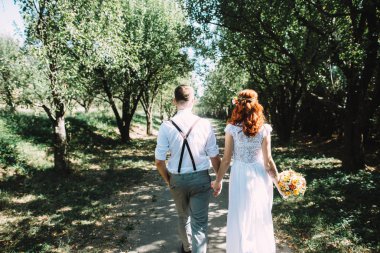 Yeni evliler bahçede yürümek ve el ele. Gelin buketi tutuyor