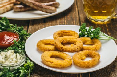 Lezzetli peynir halkaları ve ketçap, sos, maydanoz ve bira ile beyaz yuvarlak tabakta sosis