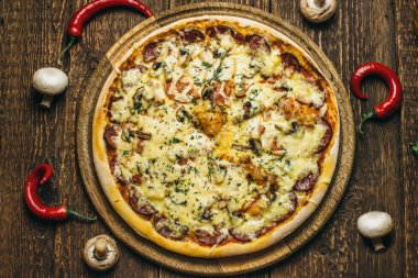 Mantar, salam, peynir, domates ve biber yuvarlak ahşap tahtası üzerinde eski bir tabloyu lezzetli pizza. Üstten Görünüm