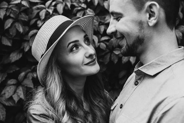 Black and white portrait of a beautiful girl in a hat and stylish guy who look at each other and smile. Close-up photo