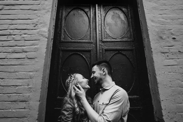 黑白照片的年轻欢快的情侣站在老墙附近 看着对方的爱和微笑 — 图库照片