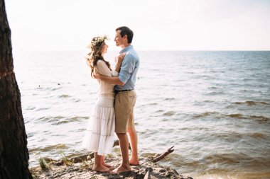 Sevgi dolu güzel bir çift günbatımında sahil üzerinde duran ve birbirine bakarak