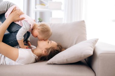 Hafta sonu evde. Mutlu anne ve küçük kızı evde birlikte eğleniyorlar kanepede uzanıyorlar ve anne sevgili bebeğini öpüyor. Mutlu annelik ve çocukluk