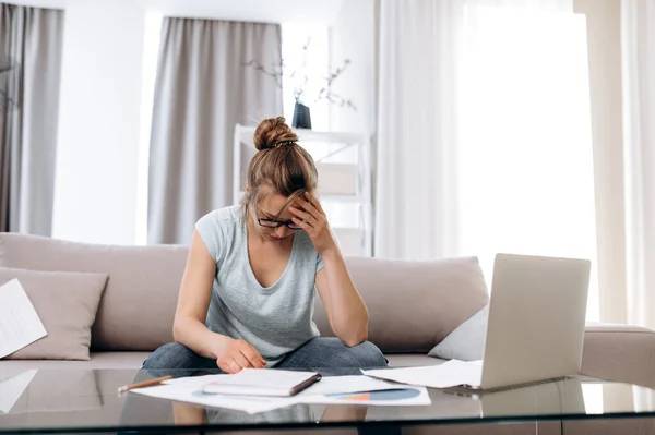 Young attractive housewife upset by utility bills, she counts family budget and pays bills online, being at home