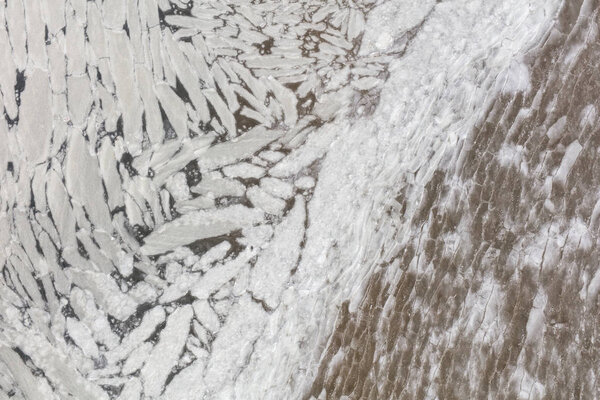 Aerial view of melting ice on the beach. Bizarre patterns of ice blocks in green water.