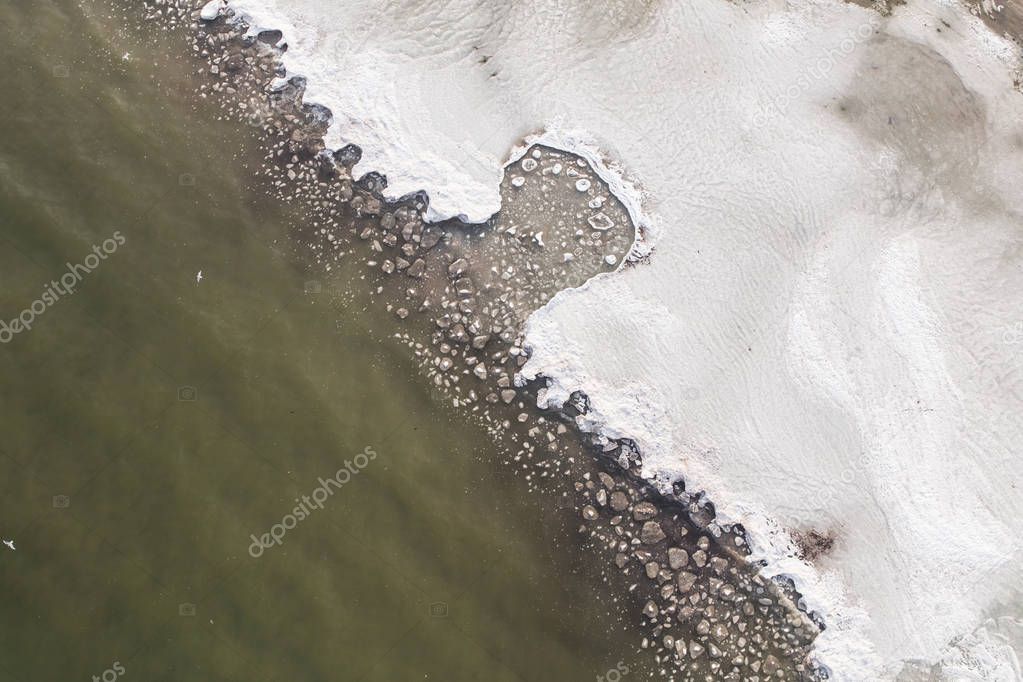 Aerial view of melting ice on the beach. Bizarre patterns of ice blocks in green water.