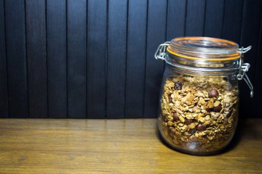 Kavanoz ve granola, müsli. Siyah ahşap arka planda kavanozda fındık bulunan ev yapımı tahıllı granola. Lezzetli ve sağlıklı kahvaltı..