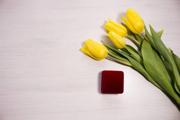 Flower tulip on white wooden background. Bouquet of the yellow tulip flowers. Valentines day concept, woman\'s day. Red gift box. Letter or invitation in a silver envelope.