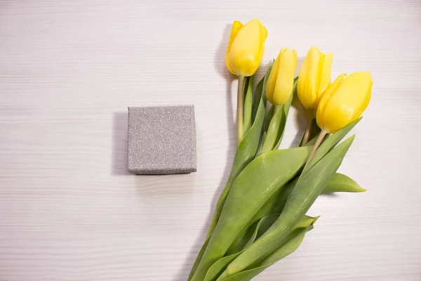 Flower tulip on white wooden background. Bouquet of the yellow tulip flowers. Valentines day concept, woman's day. Letter or invitation in a silver envelope.