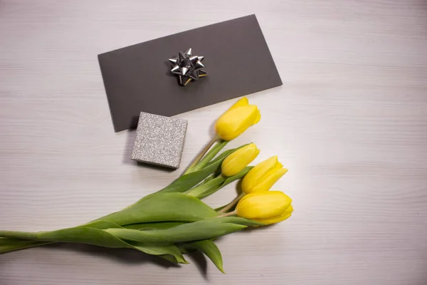 Flower tulip on white wooden background. Bouquet of the yellow tulip flowers. Valentines day concept, woman\'s day. Letter or invitation in a silver envelope.