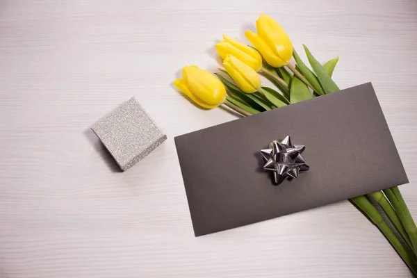 Flower tulip on white wooden background. Bouquet of the yellow tulip flowers. Valentines day concept, woman\'s day. Letter or invitation in a silver envelope.