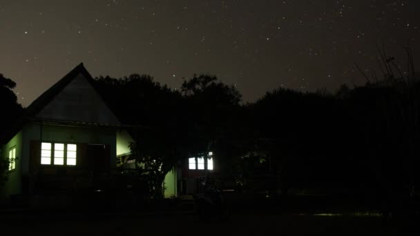 Windows でライトがオンになって 庭の木で単一階建ての家の背景に星空のタイムラプス — ストック動画