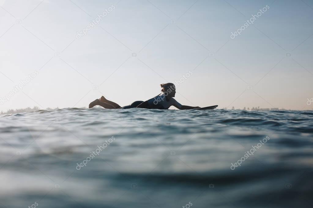 silhouette of woman lying on surf board in ocean