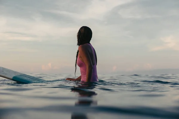 日没で水の中でサーフボードの上に座って女性サーファーのシルエット  — 無料ストックフォト