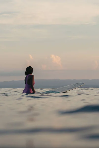 女性サーファーの日没で水の中でサーフボードの上に座っての背面図 — ストック写真