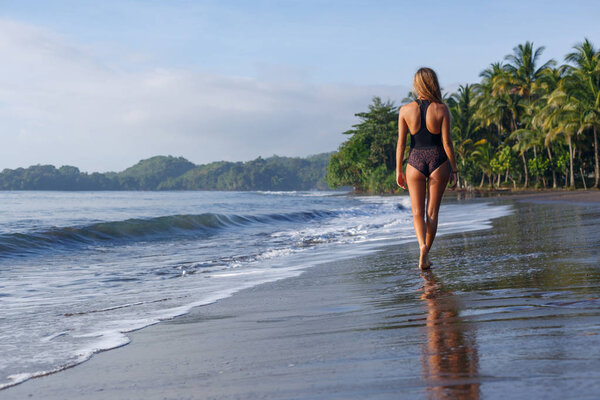 back view of young girl walking on tropical beach near ocean