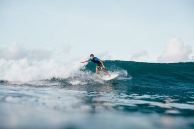 Dalgalar sörf tahtası üzerinde güneşli günde sürme wetsuit genç adam