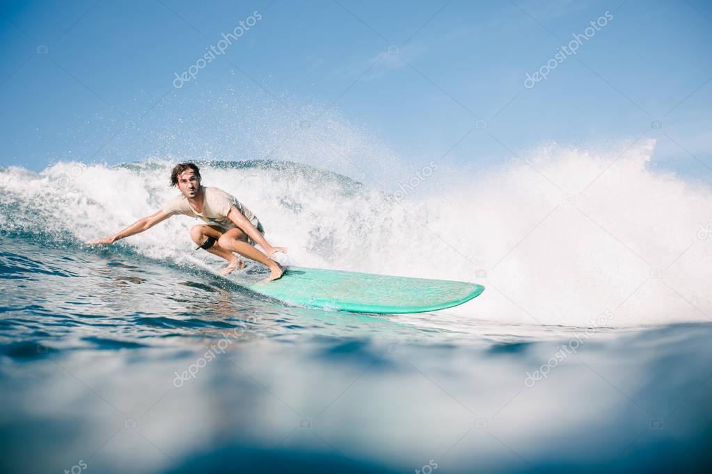 handsome man in wet t-shirt riding waves on surfboard while having vacation