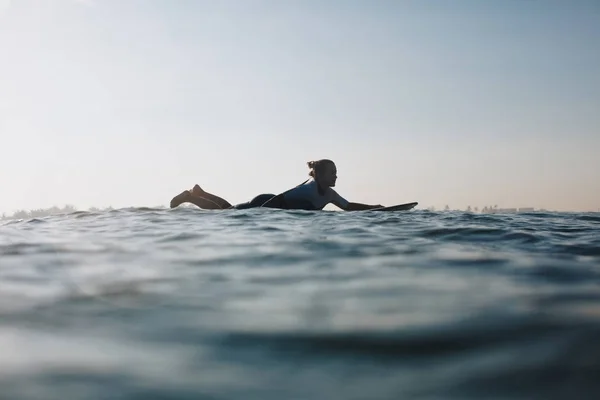 Силует жінки, що лежить на дошці для серфінгу в океані — стокове фото
