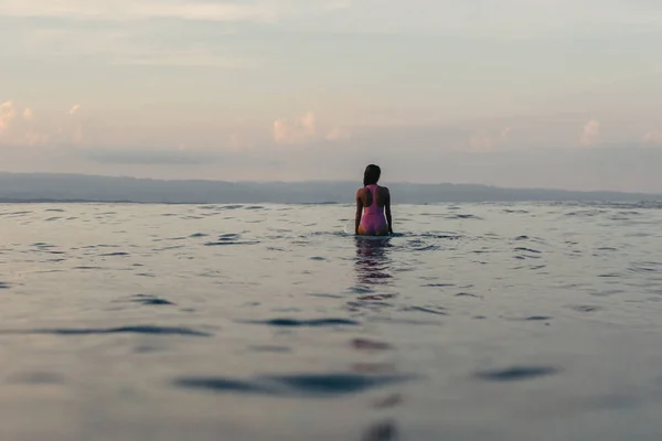 Back view of silhouette of female surfer sitting on surfboard in water — Stock Photo