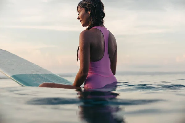 Bela mulher sentada na prancha de surf no oceano ao pôr do sol — Fotografia de Stock