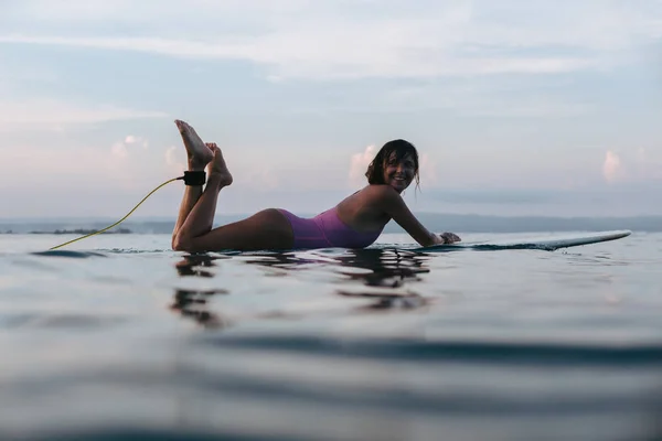 Surfista sorridente deitado na prancha de surf na água no oceano ao pôr do sol — Fotografia de Stock