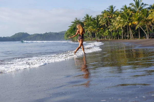 Вид сзади женщины, бегущей по пляжу у океана — стоковое фото