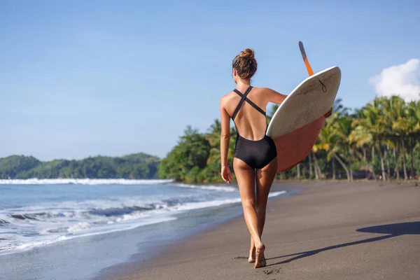 Visão traseira do jovem surfista caminhando com prancha na praia — Fotografia de Stock