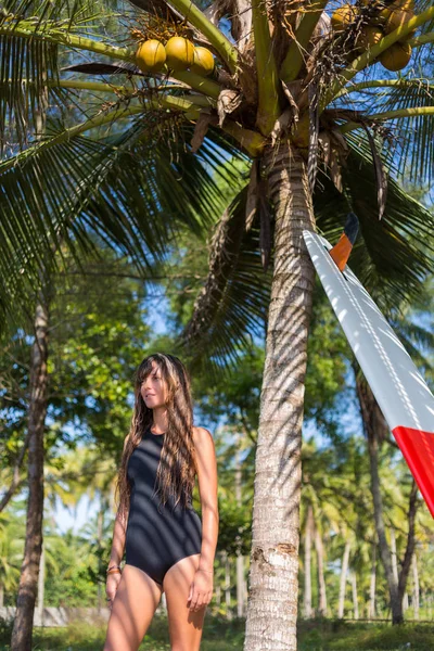 Joven surfista posando con tabla de surf cerca de la palmera - foto de stock