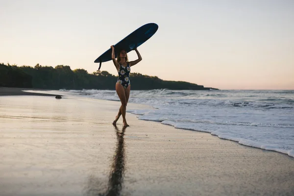 Sportive en maillot de bain avec planche de surf bleue marchant sur la plage — Photo de stock