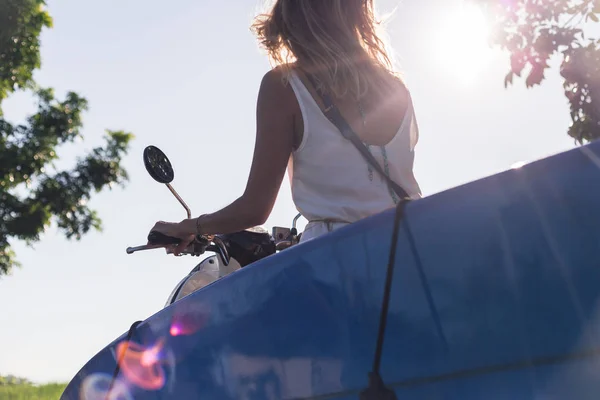 Visão parcial da mulher montando scooter com prancha de surf contra o céu azul — Fotografia de Stock