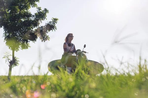 Young woman riding scooter with surfing board — Stock Photo