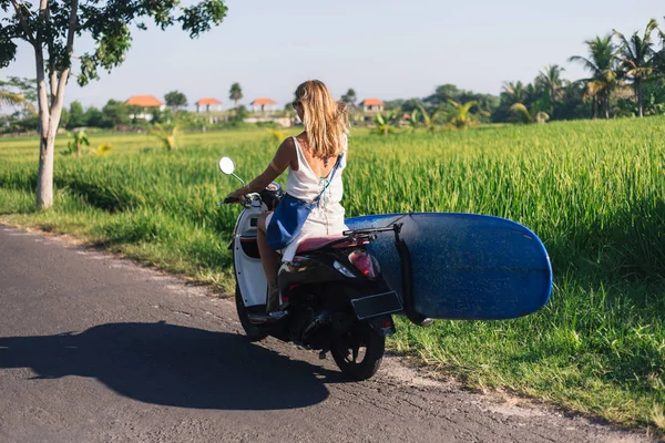 Rear view of woman riding scooter with surfing board — Stock Photo