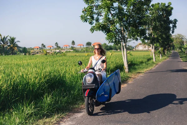 Jovem sorrindo mulher montando scooter com prancha de surf — Fotografia de Stock