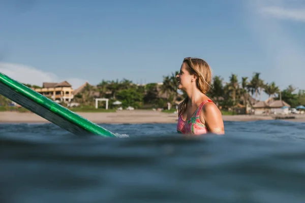 Seitenansicht einer jungen Frau im Badeanzug, die auf einem Surfbrett im Ozean ruht, mit Küstenlinie im Hintergrund — Stockfoto