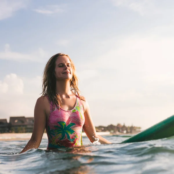 Portrait of young woman in swimming suit resting on surfing board in ocean — Stock Photo