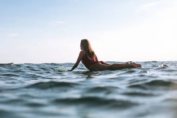 Frau in Badeanzug liegt an sonnigem Tag auf Surfbrett im Meer — Stockfoto