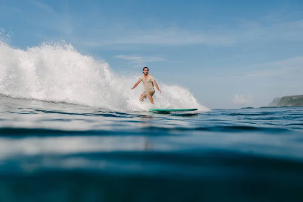 Vista lateral del joven en camiseta mojada montando olas en la tabla de surf - foto de stock