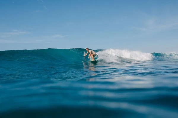 Jeune homme en t-shirt mouillé chevauchant les vagues bleues sur planche de surf tout en ayant des vacances — Photo de stock