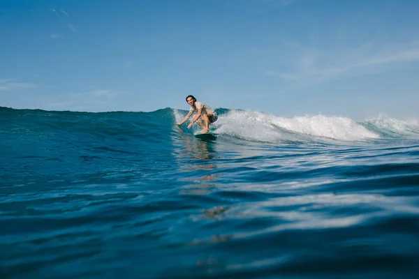 Hombre atlético en camiseta mojada montando olas en la tabla de surf en el día soleado - foto de stock