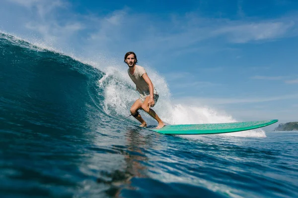 Jeune homme en t-shirt mouillé chevauchant les vagues sur planche de surf le jour ensoleillé — Photo de stock