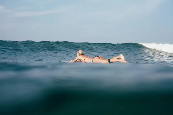 Young woman in bikini swimming on surfboard — Stock Photo