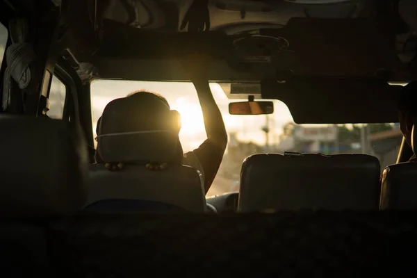 beautiful sunset shot from the inside of a car, Vietnames bus traveling with golden light, driver is raising his hand to flip down the sun shield