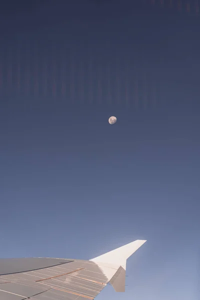 Vleugel van het vliegtuig door het vliegtuigraam met de maan op de achtergrond — Stockfoto