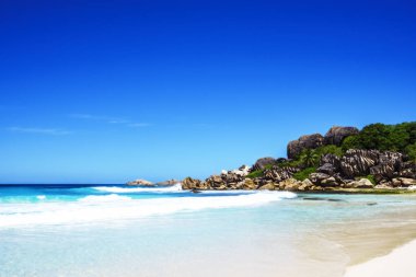 Beyaz kum, palmiye ağaçları, Granit kayalar ve turkuaz su