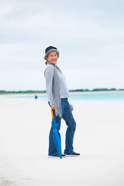 Vriendelijke volwassen vrouw met paraplu oceaan achtergrond — Stockfoto