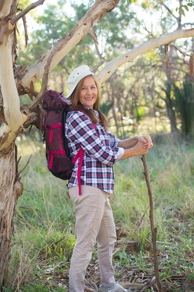Happy Mature woman hiking with backpack and stick